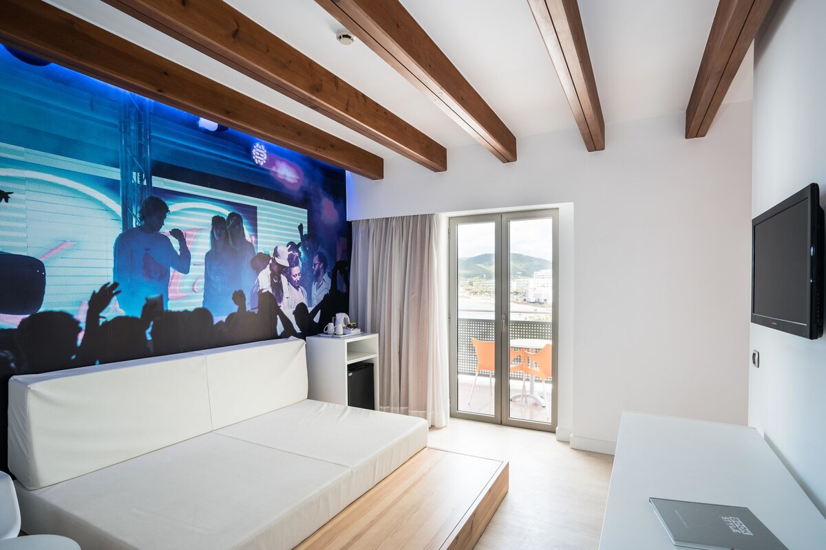 A modern hotel room with a large bed, a TV mounted on the wall, and a balcony with a view.