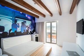 Habitación de hotel moderna con una cama grande, un televisor montado en la pared y un balcón con vistas.