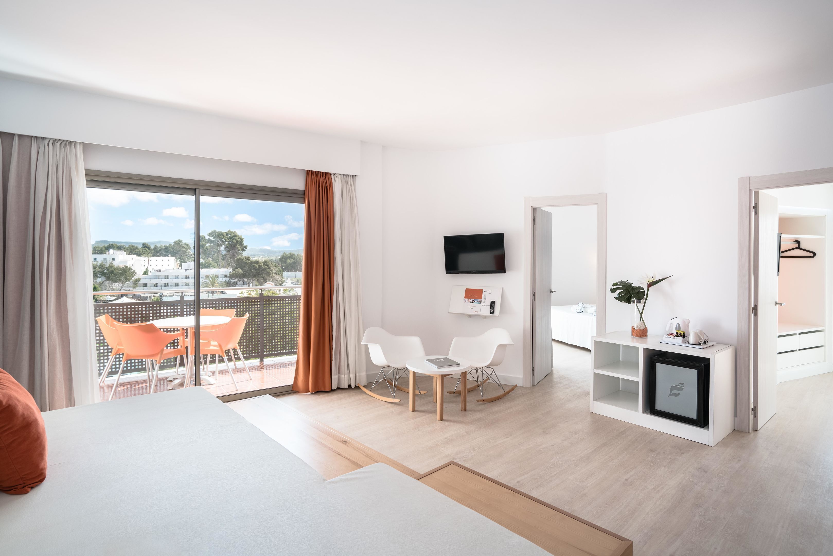 A modern hotel room with a balcony, a TV, a desk, and a wardrobe.
