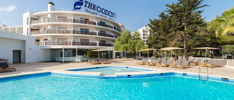 Un hotel THOcean con piscina, sillas de descanso y un cielo azul despejado.