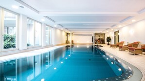 Una piscina interior amb aigua blava cristal·lina, envoltada per un paviment de rajoles i parets blanques. Hi ha finestres d'un costat, que deixen entrar llum natural.