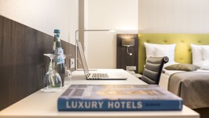 Una habitació d'hotel amb un llit, un escriptori amb un ordinador portàtil, un llibre anomenat 'Luxury Hotels' i una ampolla d'aigua.