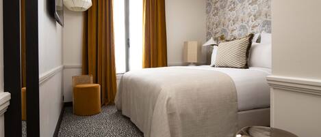 A hotel room with a bed, a chair, a lamp, and a patterned floor.