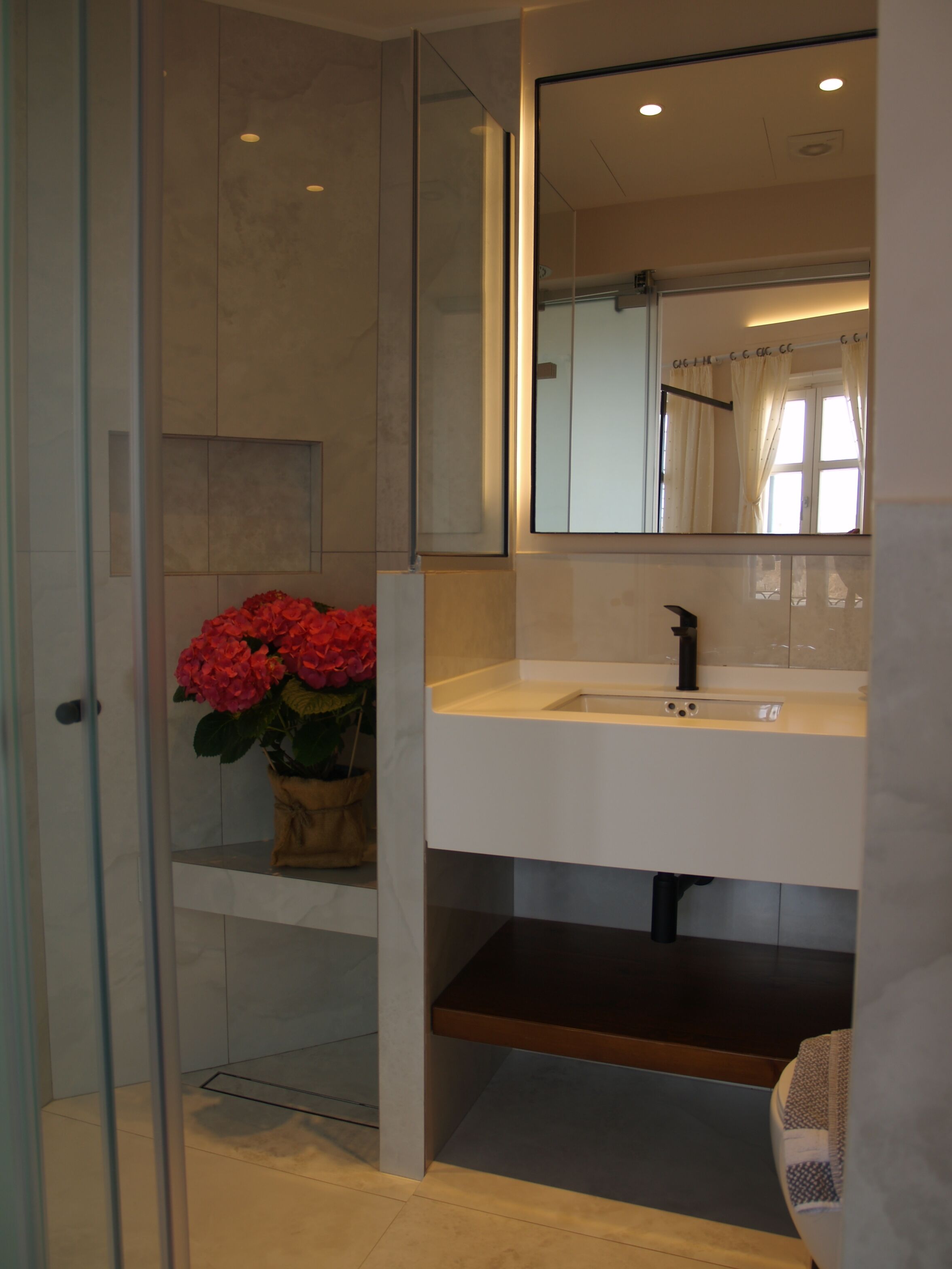 A modern bathroom with a glass shower enclosure, a white sink, and a mirror above it.