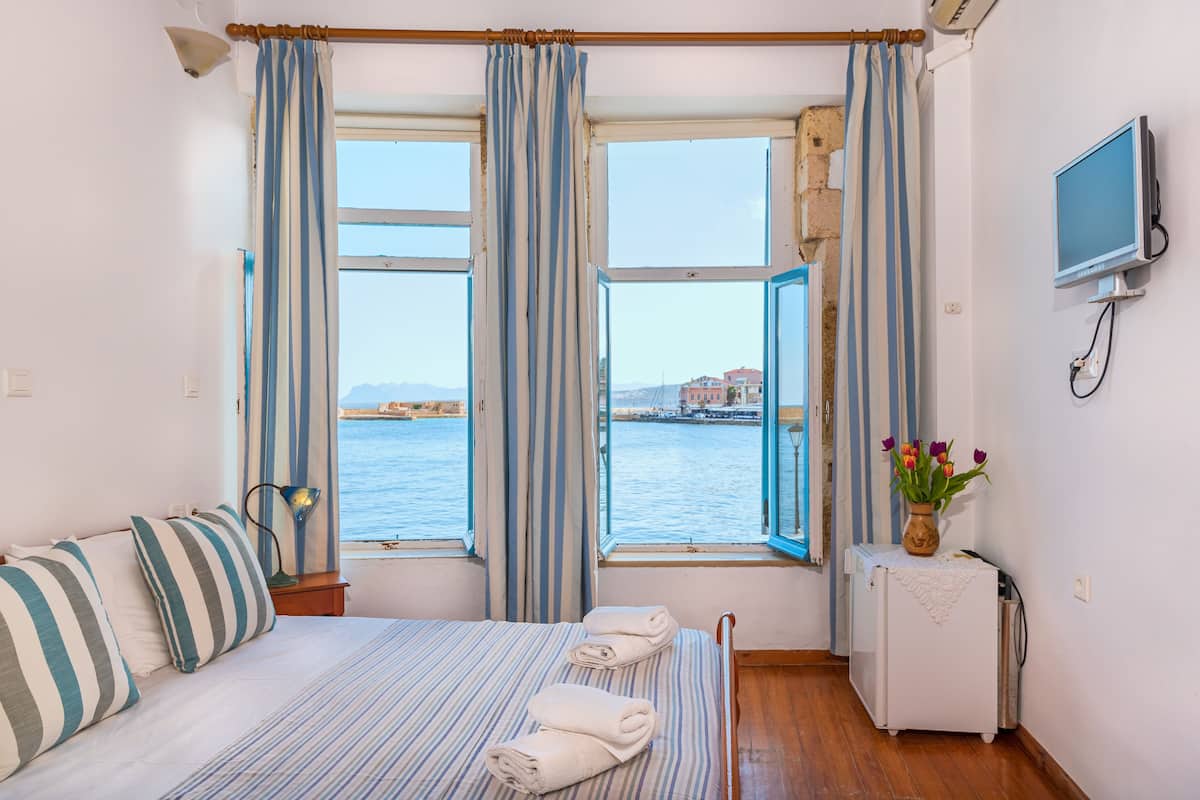A hotel room with a bed, a small table with a vase of flowers, a TV, and a view of the sea.