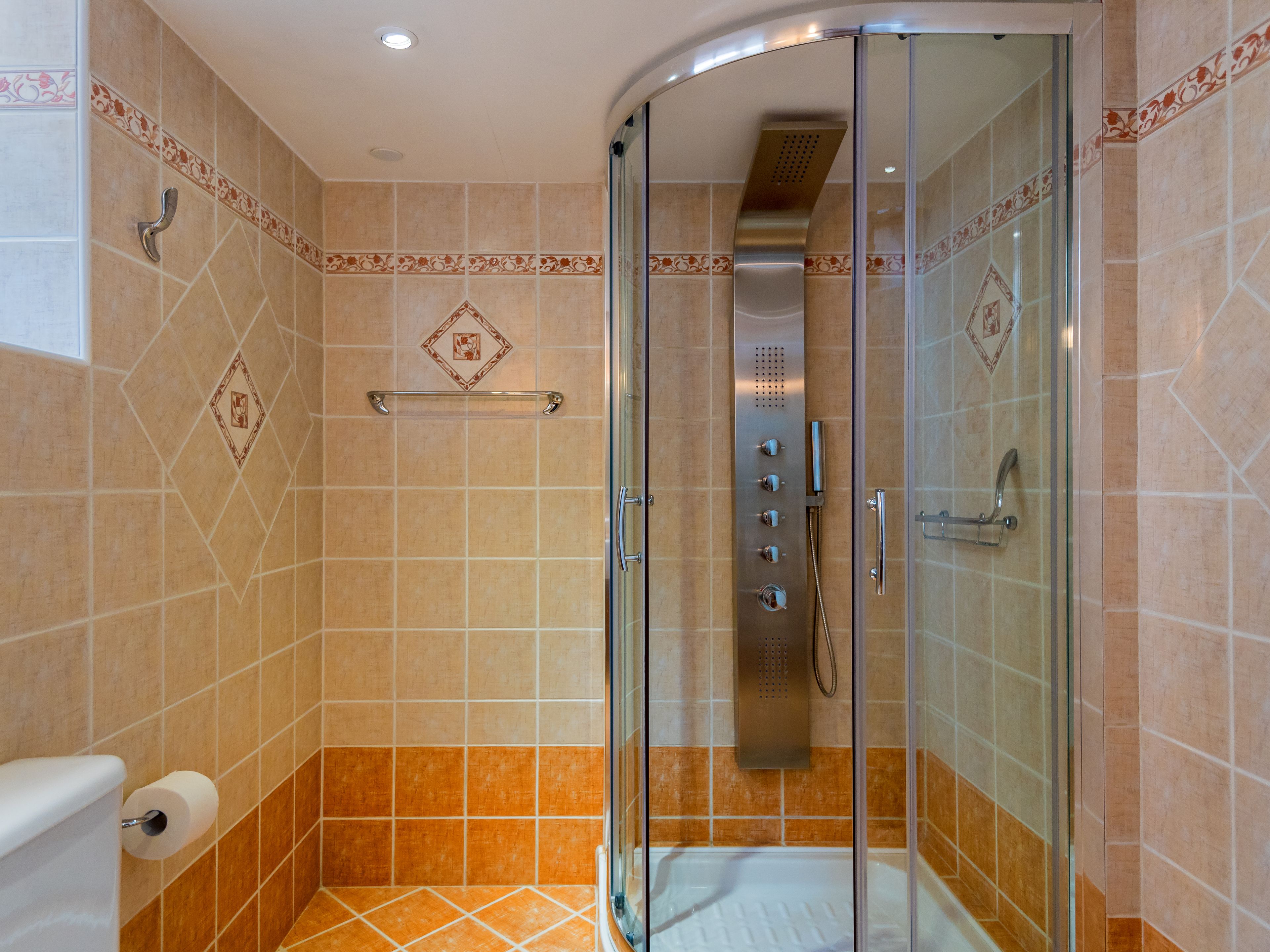 A glass-enclosed shower with a control panel, a towel rack, and a toilet with a paper towel holder.