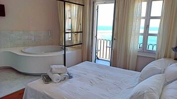 Un dormitorio con una cama grande, una bañera y un balcón con vistas al mar.