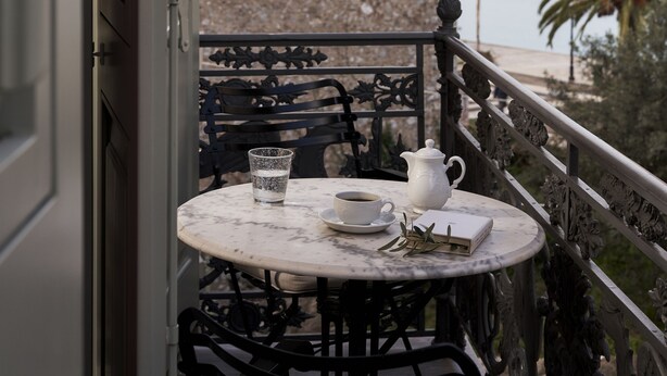 Un balcón con una mesa para dos personas, una jarrón blanco, una taza y un libro.