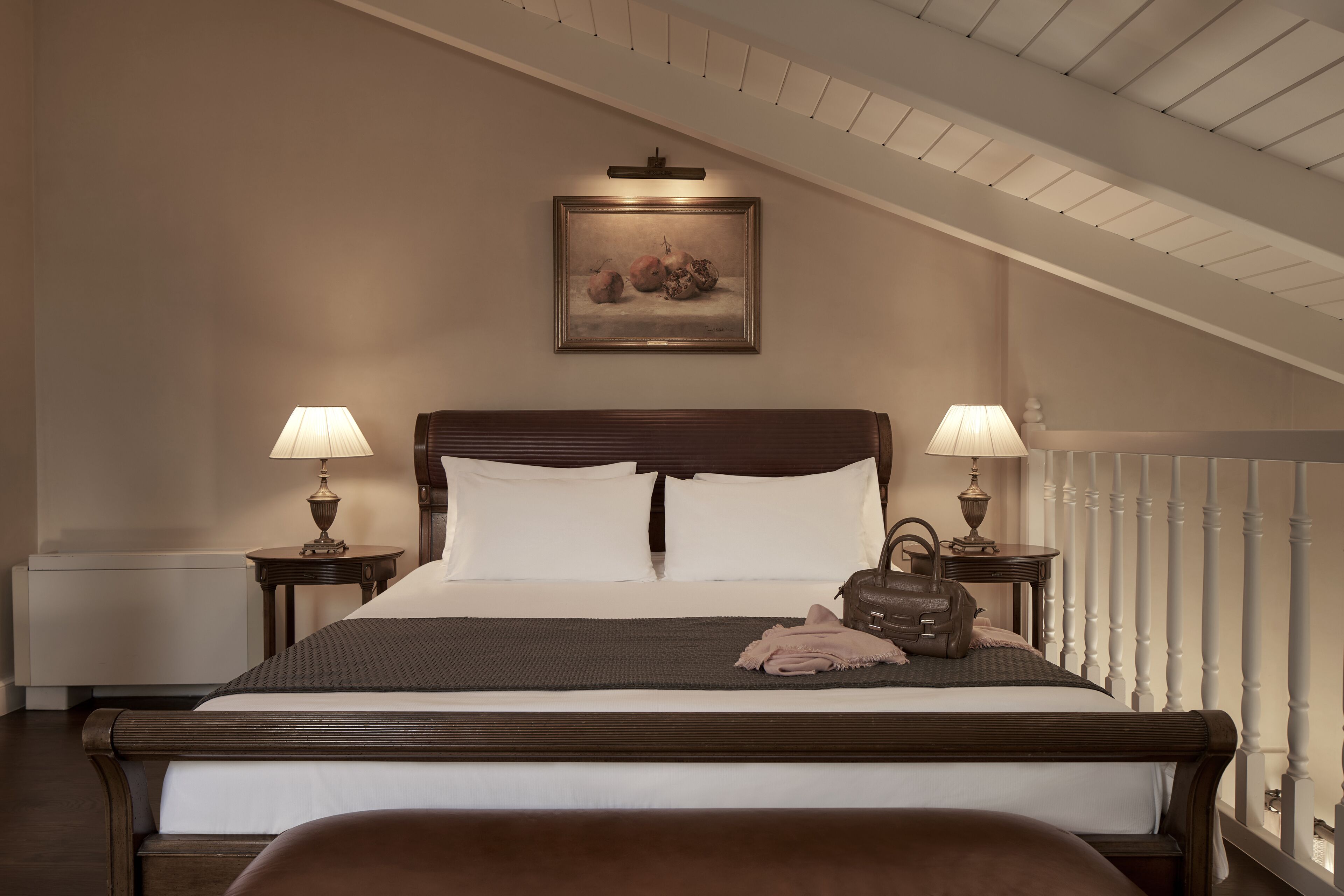 A neatly made bed with a headboard, two bedside lamps, a framed artwork above, and a radiator below.