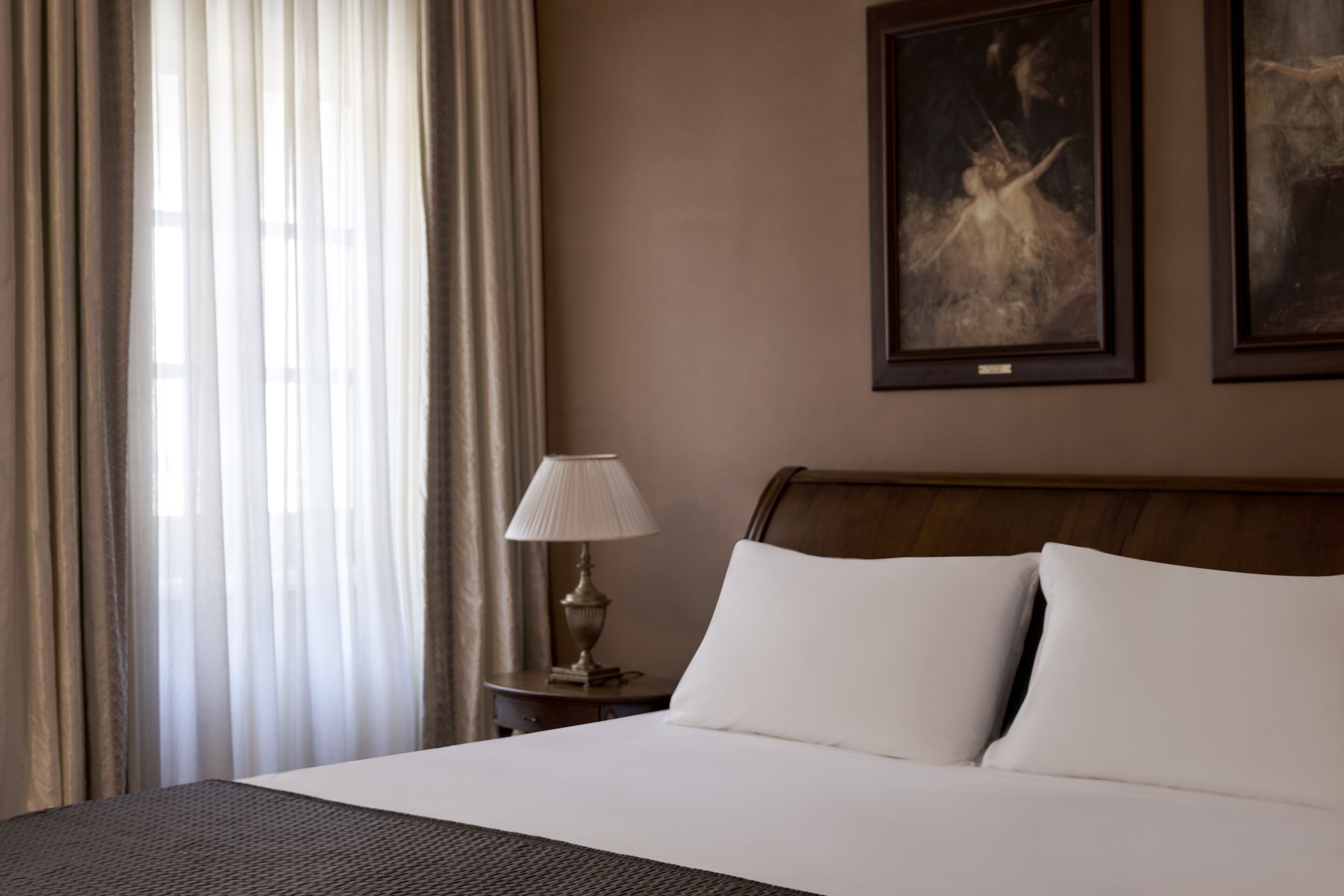 A hotel room with a large bed, a nightstand with a lamp, and two framed pictures on the wall.
