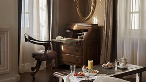 Una habitación con un escritorio de madera, una silla, un espejo y una mesa dispuesta para el desayuno, con huevos, tostadas y un vaso de jugo.