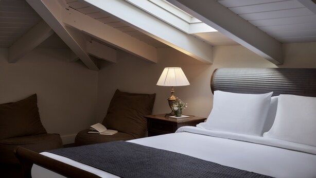 A hotel room with a skylight, a bed, a nightstand with a lamp, and a chair. - Ippoliti Hotel (Nafplio)