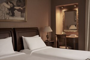 Un cuarto de hotel con una cama grande, una mesita de noche con lámpara, una silla, un escritorio con espejo y un cuadro en la pared.