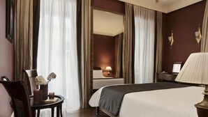 Habitación de hotel con una cama grande, una mesita de noche con lámpara, una silla, una pequeña mesa con un florero y un espejo grande en la pared.
