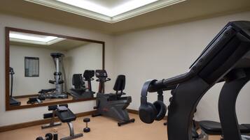 A gym with exercise equipment, a bench, dumbbells, and a large mirror.