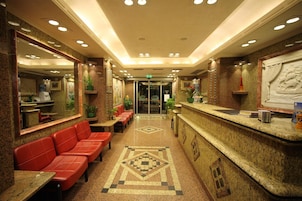 Vestíbulo de hotel con una mesa de recepción, asientos de cuero rojo y piso con diseño.