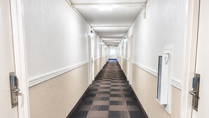 A long, narrow hotel corridor with checkered carpet, white walls, and doors on both sides. - Motel 6 New Stanton, PA (New Stanton)