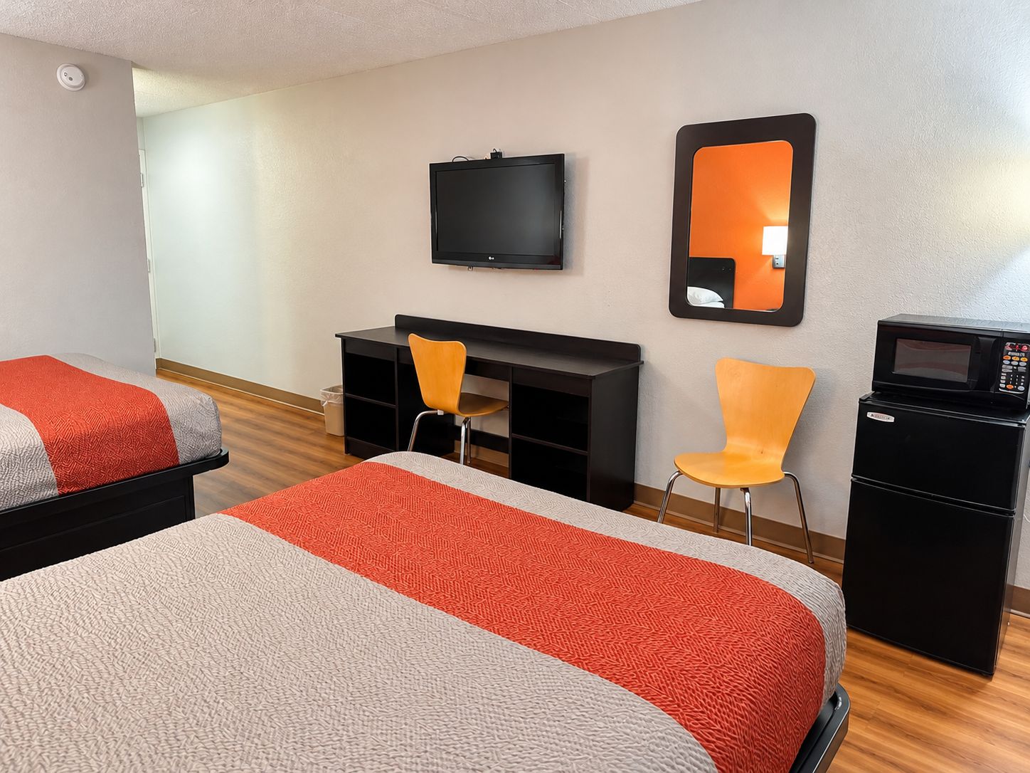 Una habitación de hotel con dos camas, un escritorio, una silla, un televisor, un espejo y un microondas.