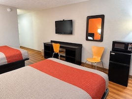A hotel room with two beds, a desk, a chair, a television, a mirror, and a microwave.