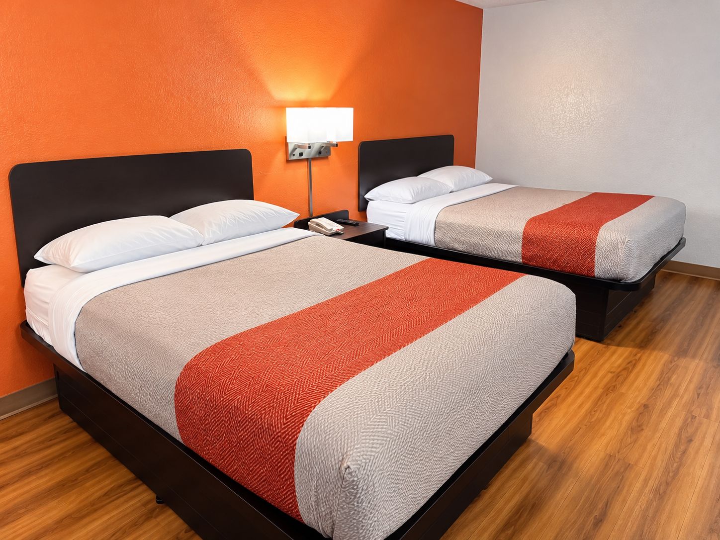 Une chambre d’hôtel avec deux lits, une table de chevet avec une lampe et un plancher en bois.