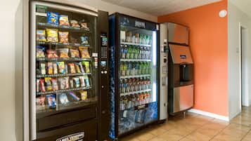 Deux distributeurs automatiques, l’un proposant des en-cas et l’autre des boissons, se trouvent dans une pièce aux murs orange et au sol carrelé.