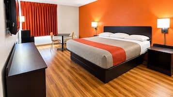A hotel room with a bed, bedside tables, a desk, a chair, a television, and orange curtains.