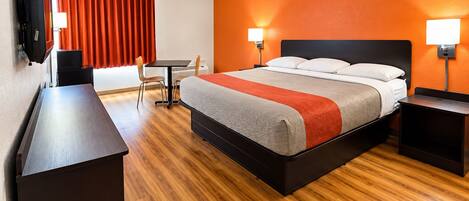 Habitación de hotel con cama, mesitas de noche, escritorio, silla, televisión y cortinas anaranjadas.