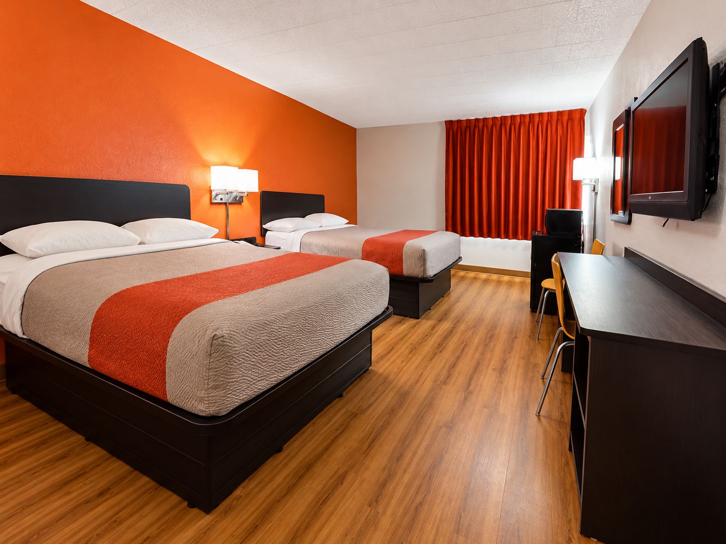 Une chambre d’hôtel avec deux lits, un bureau, une chaise, une télévision et une fenêtre avec des rideaux.