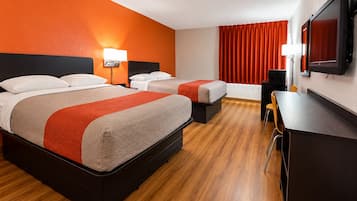 Une chambre d’hôtel avec deux lits, un bureau, une chaise, une télévision et une fenêtre avec des rideaux.