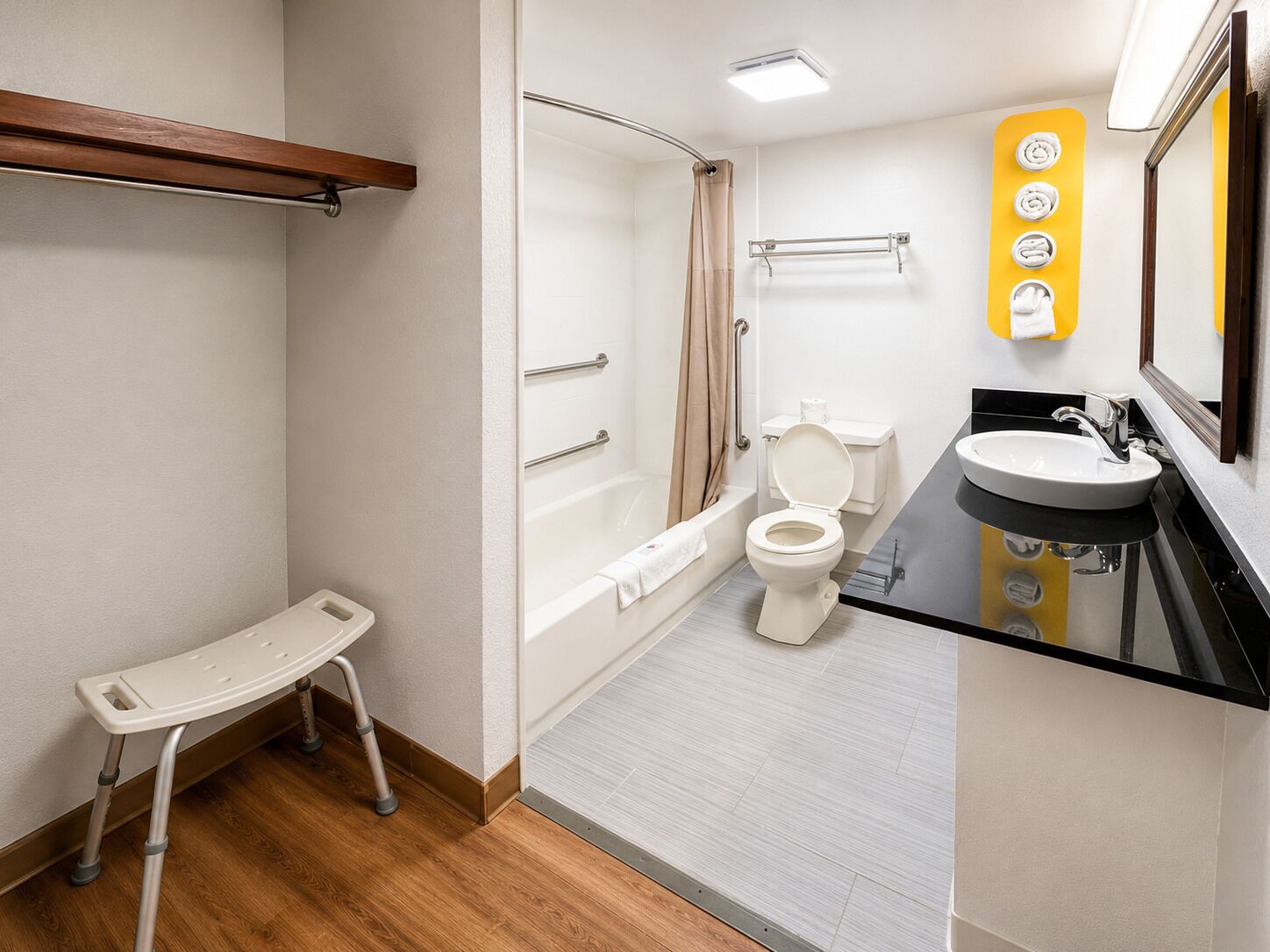 A bathroom with a shower, toilet, and sink, equipped with grab bars and a wheelchair-accessible bench.