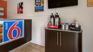 A motel lobby with a reception desk, a television mounted on the wall, and a coffee station with Folgers coffee and Njoy creamer. - Motel 6 New Stanton, PA (New Stanton)