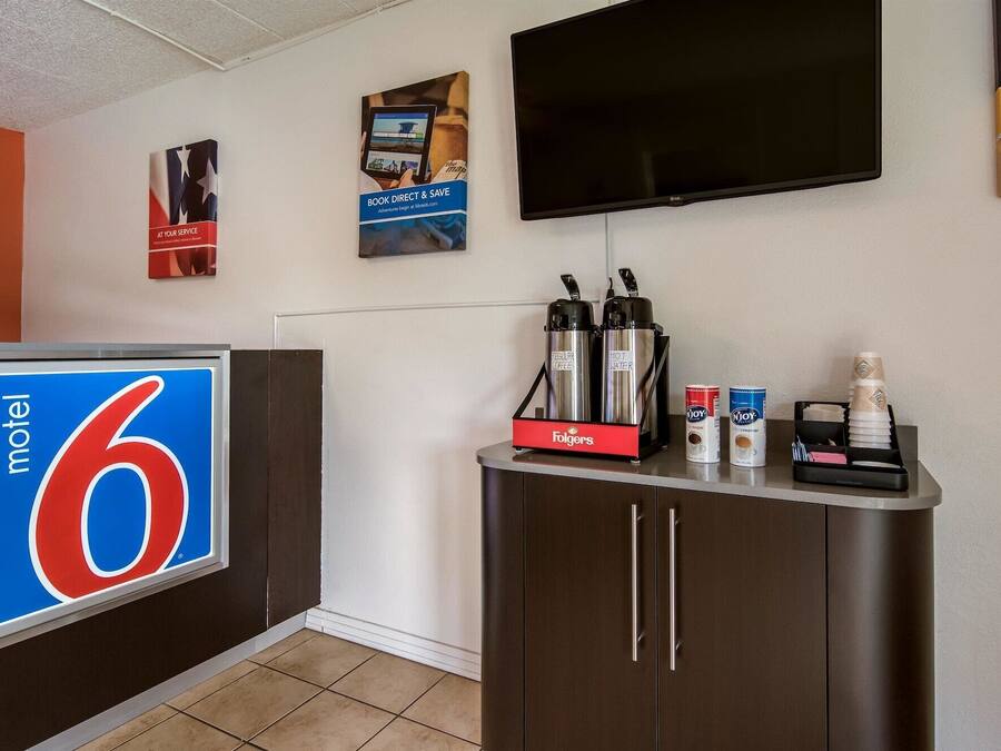A motel lobby with a reception desk, a television mounted on the wall, and a coffee station with Folgers coffee and Njoy creamer.