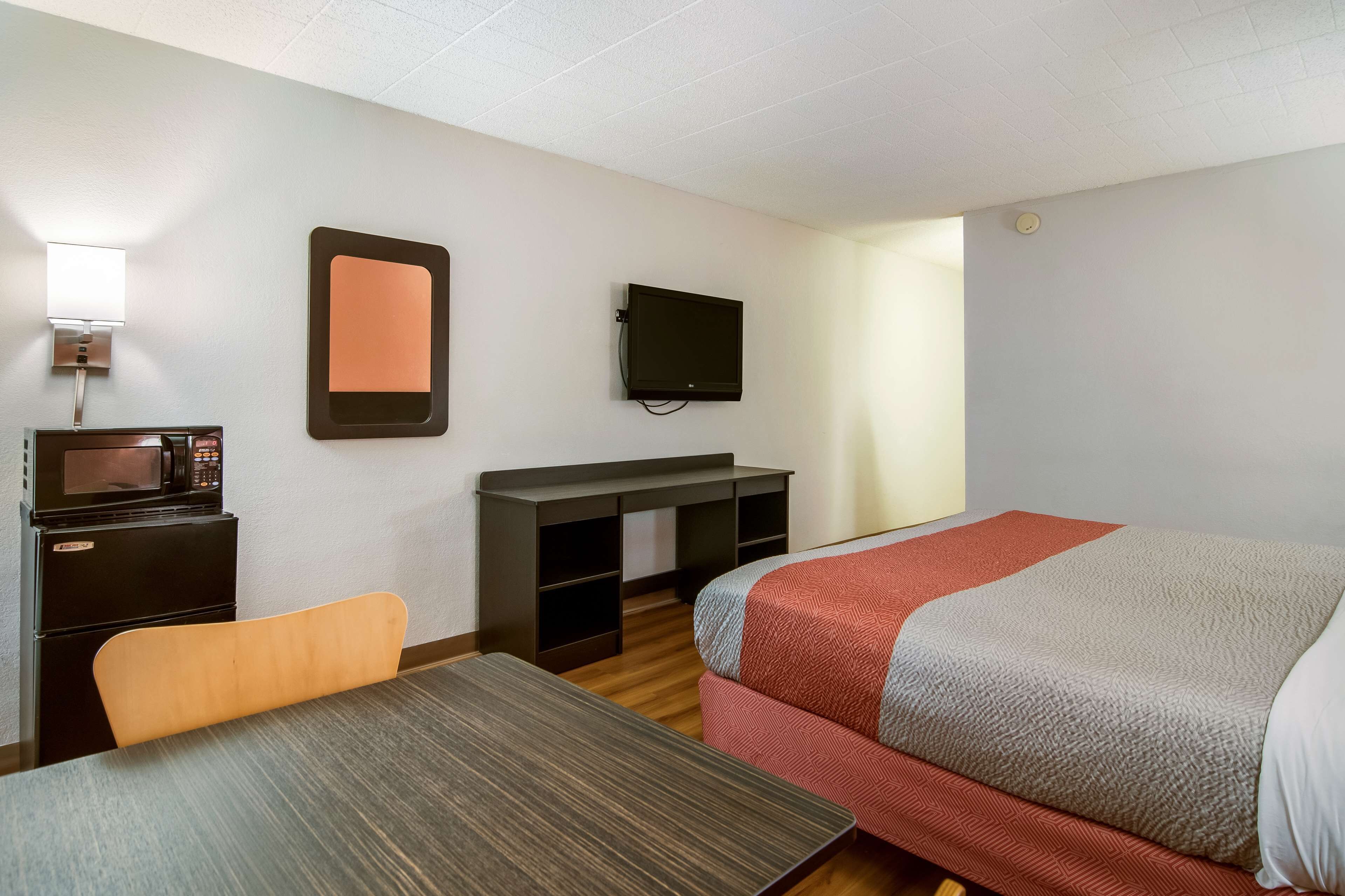 Habitación de hotel con una cama, un escritorio con silla, microondas, televisión y una mesita.