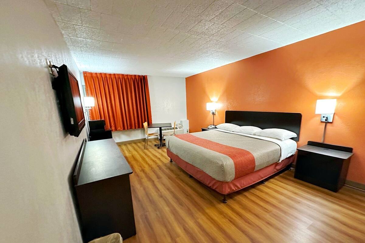 Una habitación de hotel con cama, escritorio, silla, cesto de basura y dos lámparas de noche.