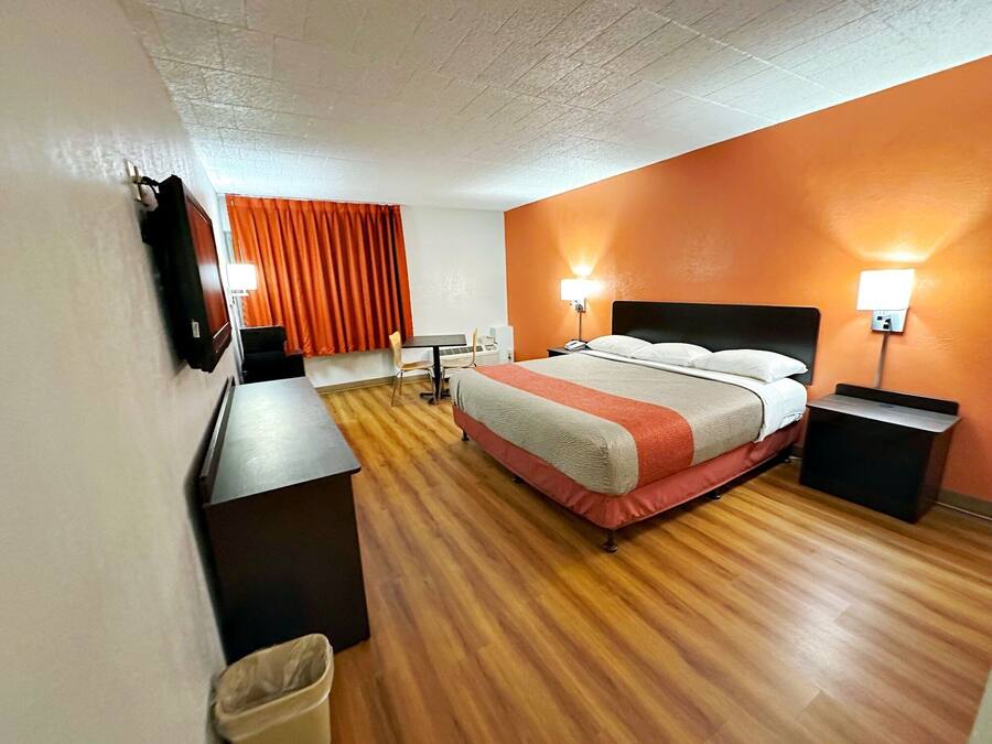 Quarto de hotel com cama, escrivaninha, cadeira, lixeira e duas luminárias de cabeceira.