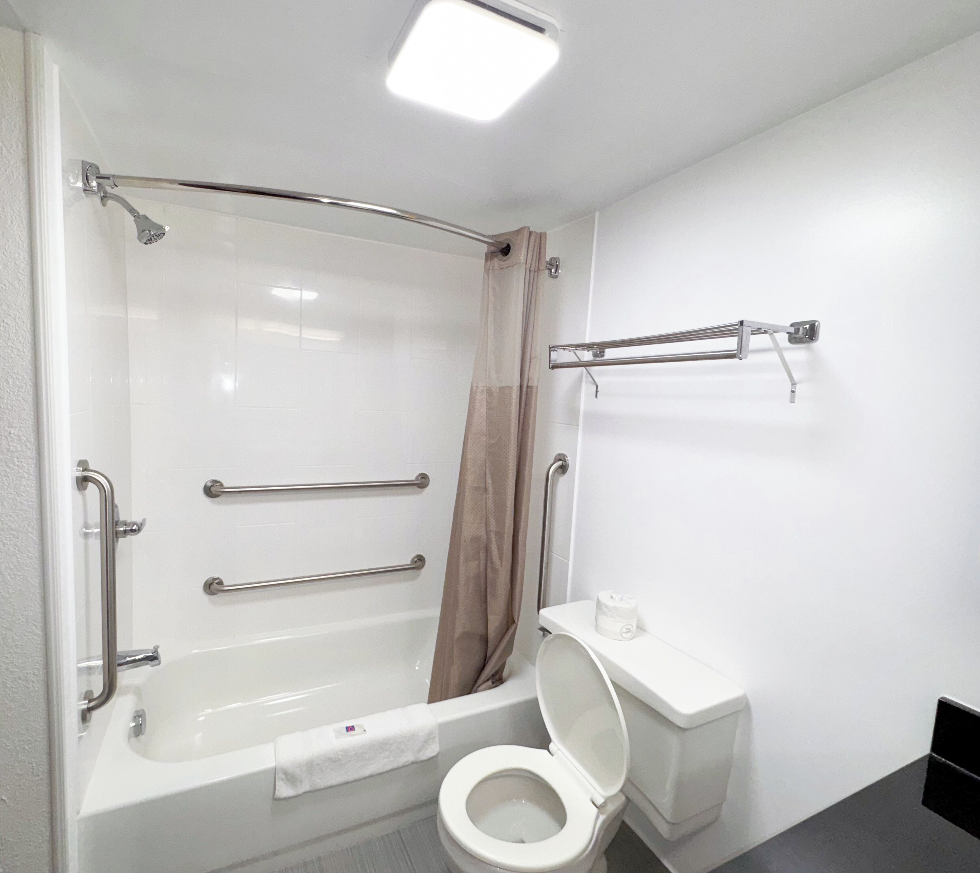 A modern bathroom with a walk-in shower, grab bars, a toilet, and a towel rack.