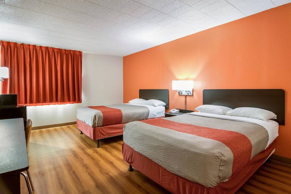 Habitación de hotel con dos camas, un escritorio y una ventana con cortinas rojas.