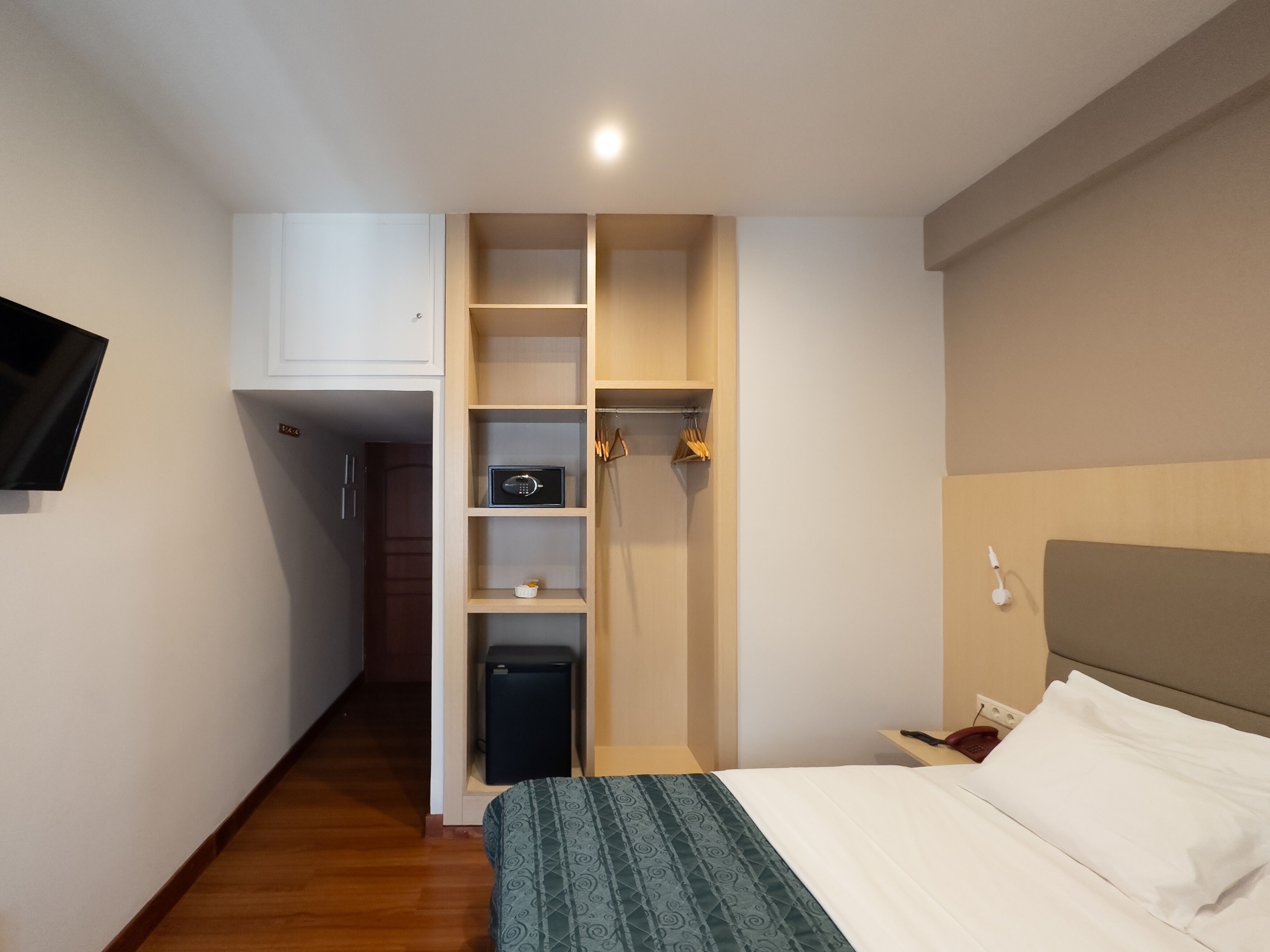 Ein Hotelzimmer mit einem Bett, einem Kleiderschrank, einem kleinen Schreibtisch und einem an der Wand befestigten Fernseher.