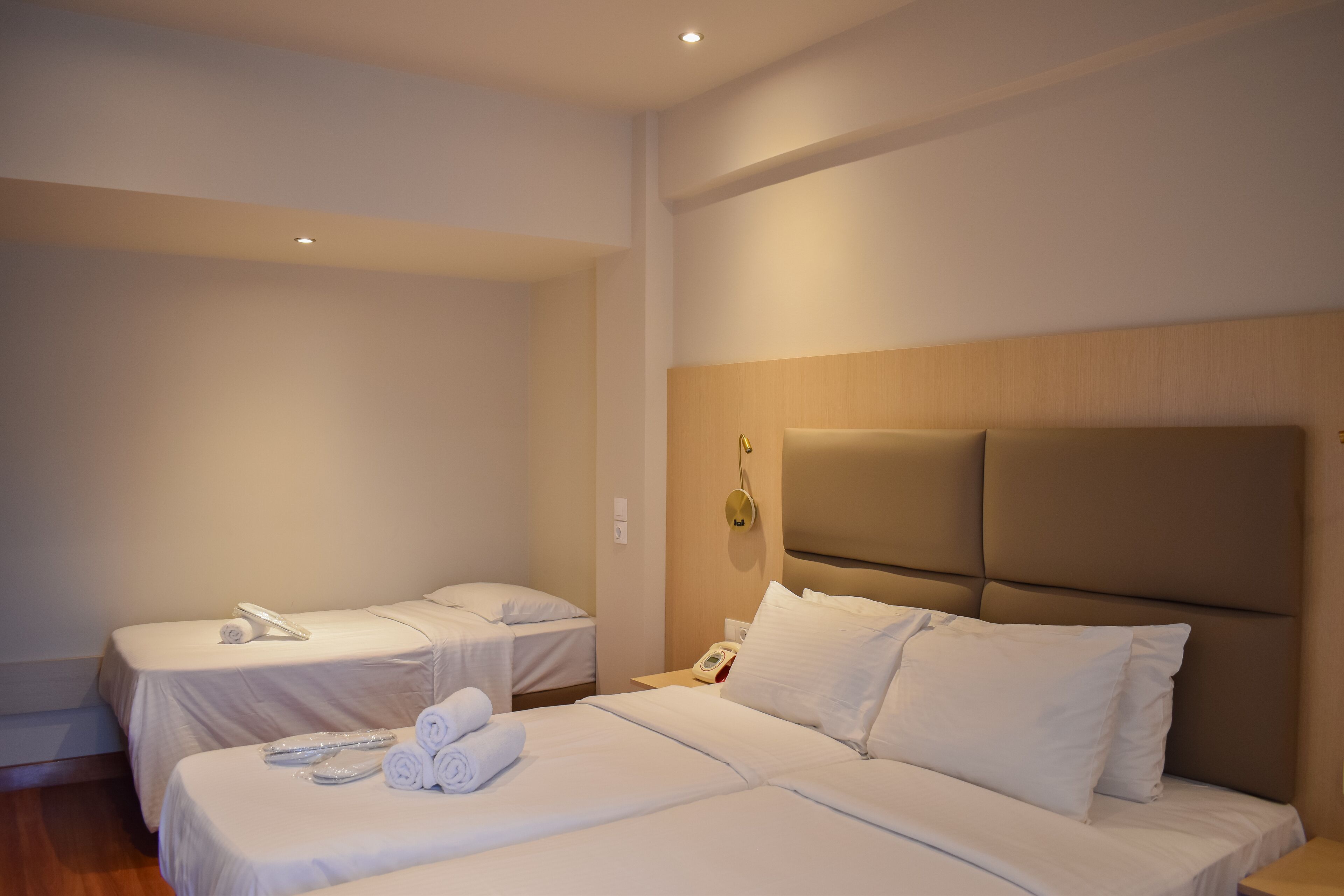 A hotel room with two beds, a wooden headboard, and a bedside table with a phone.