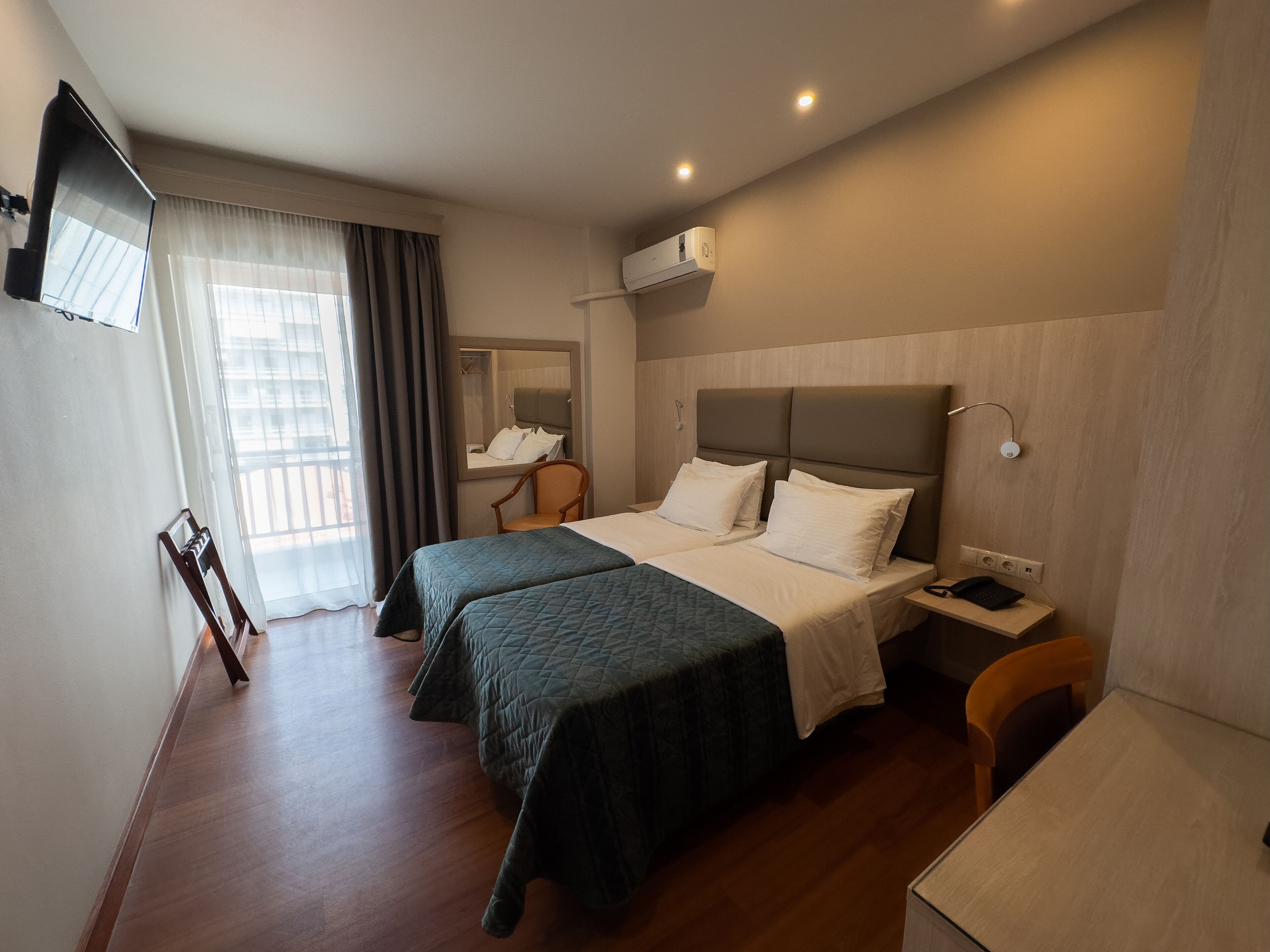 A hotel room with two beds, a desk, a chair, a TV, and a window with curtains.