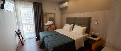 A hotel room with two beds, a desk, a chair, a TV, and a window with curtains.
