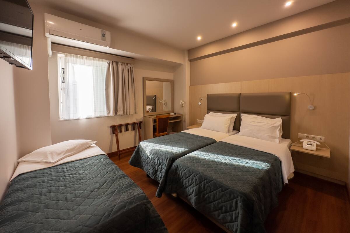 A hotel room with two single beds, a desk, a chair, a mirror, and a window with curtains.