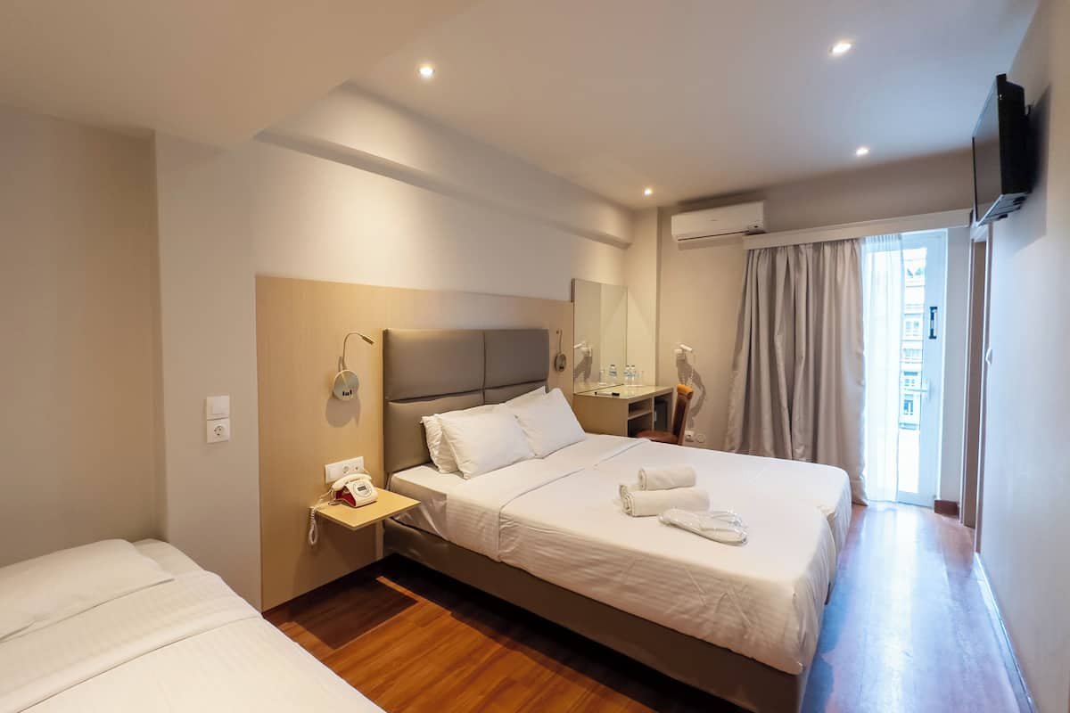 A hotel room with a large bed, a smaller bed, a bedside table with a phone, a mirror, and an air conditioning unit.