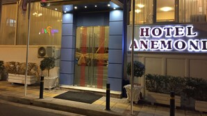 A hotel entrance with a large illuminated sign, a glass door, and a small entrance mat. - Anemoni (Piraeus)