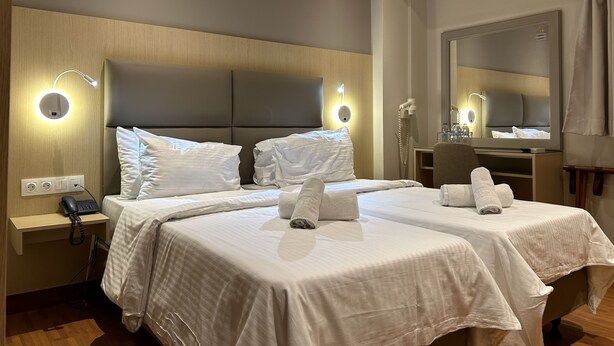 A hotel room with two beds, a desk, a chair, a mirror, and a phone on the nightstand. - Anemoni (Piraeus)