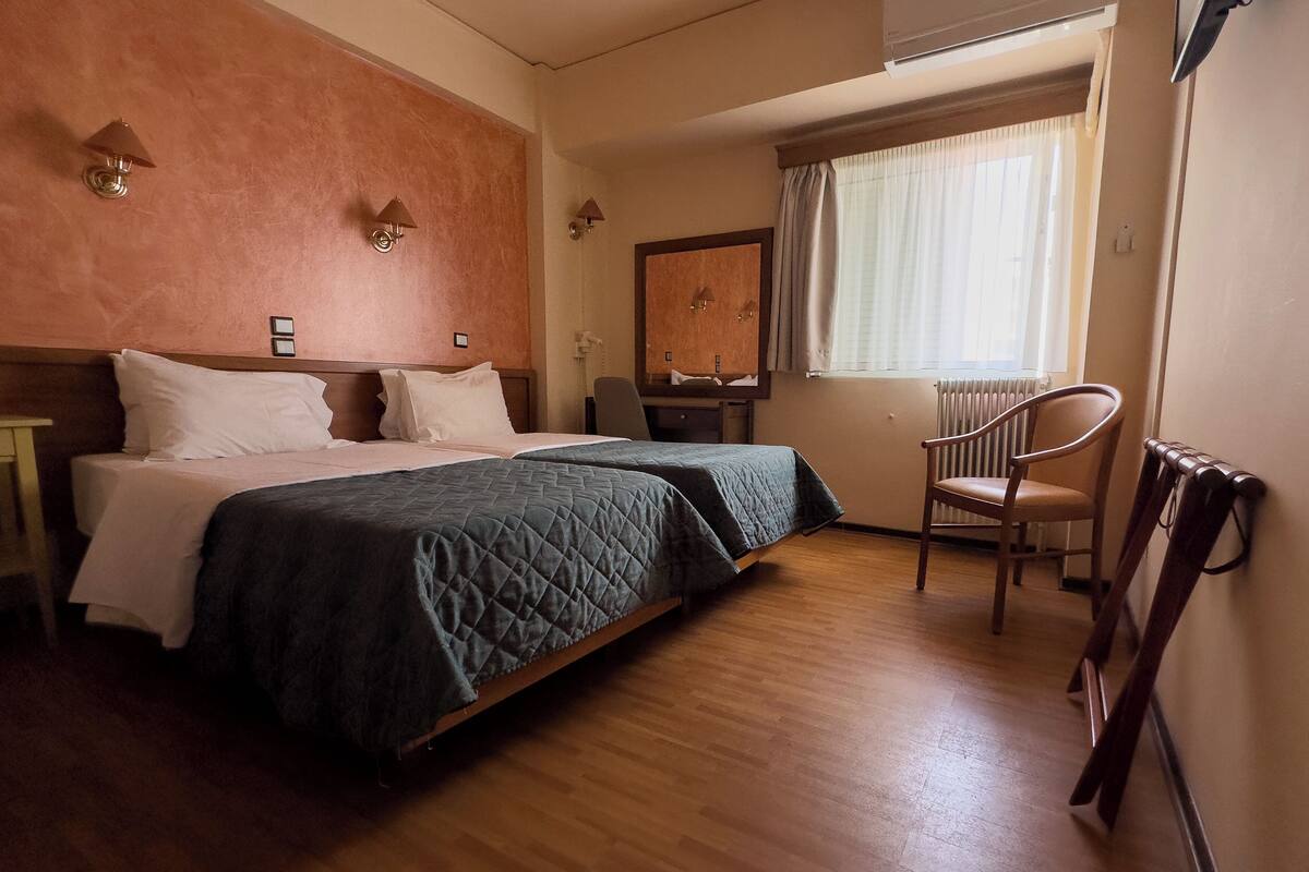 A hotel room with a large bed, a chair, a desk, and a window with curtains.