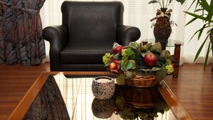 A living room with a black leather sofa, a glass coffee table, a decorative basket with fruits and flowers, and a vase with plants. - Anemoni (Piraeus)
