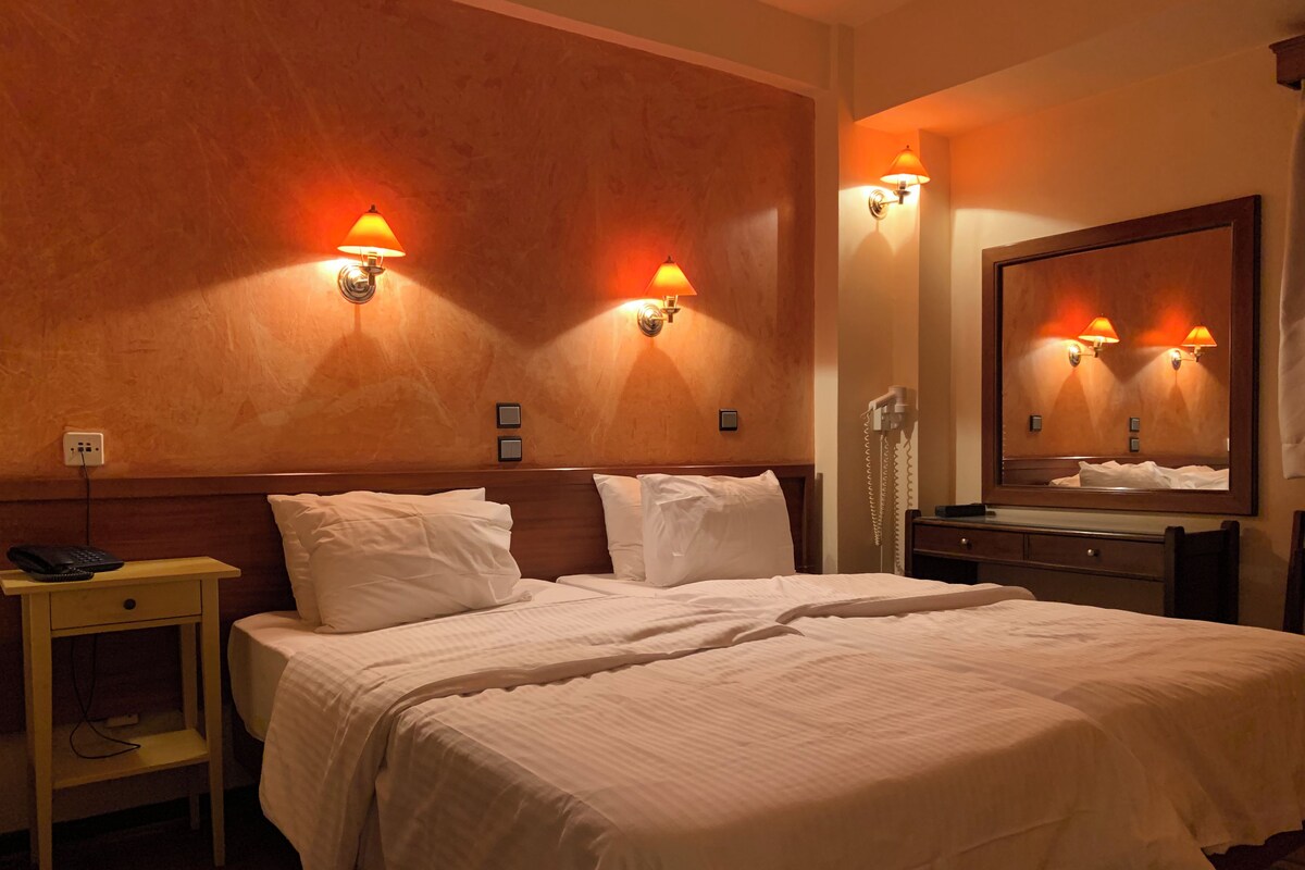 A hotel room with a large bed, two bedside tables, a nightstand, a telephone, and wall-mounted lamps.