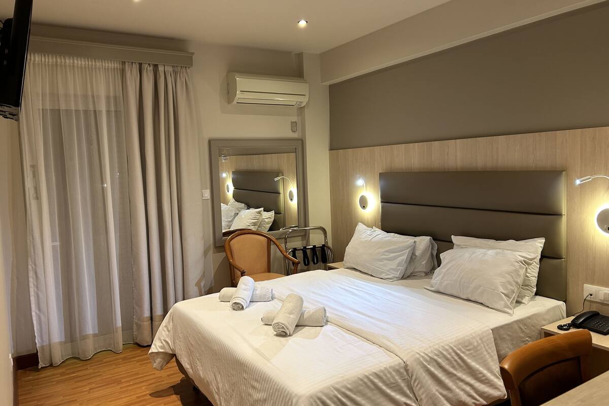 A hotel room with a large bed, a chair, a desk, and an air conditioning unit.