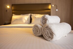 A neatly made bed with rolled white towels, a wooden headboard, and a wall-mounted light fixture. - Anemoni (Piraeus)